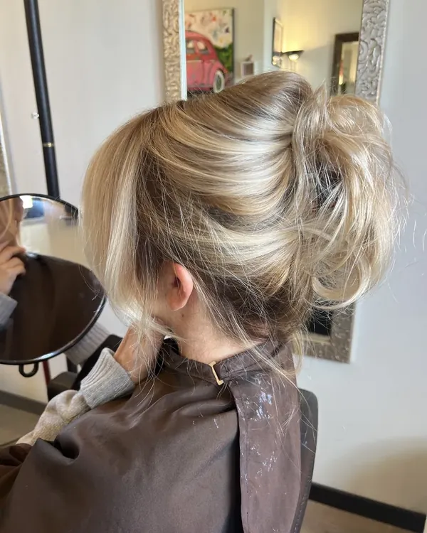 Getextureerd blond opsteekkapsel met zachte highlights en losse lokken langs het gezicht